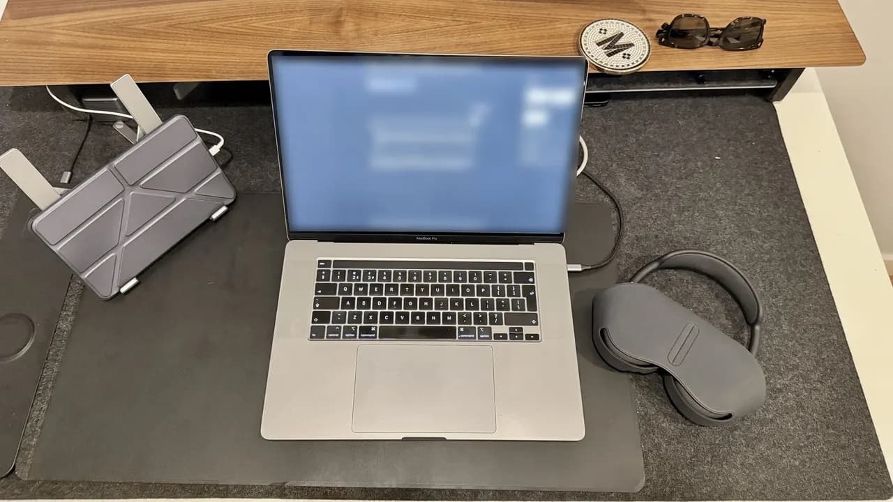 My desk from above: a laptop with its screen blurred, a tablet stand and a pair of headphones.